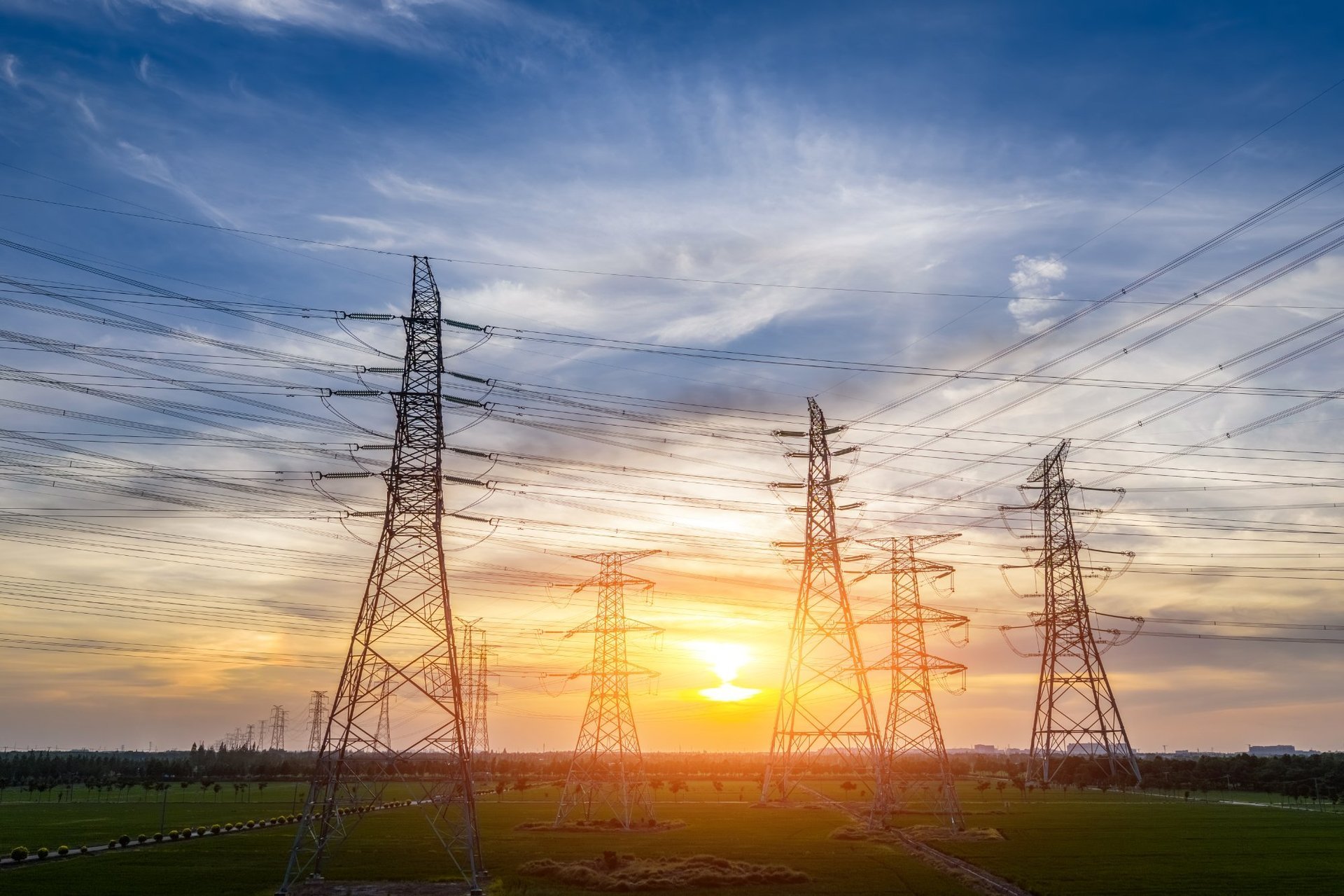 High-voltage transmission towers over green fields at sunset